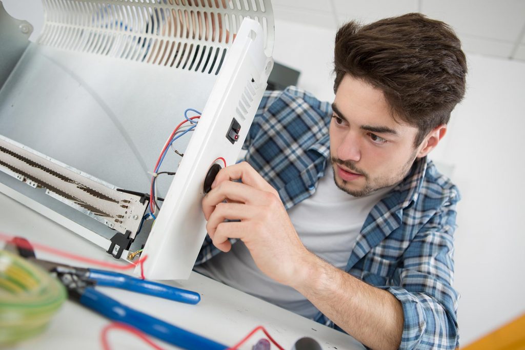 young male plumber examining electric heater